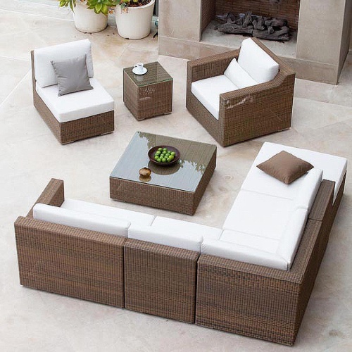 70259 malaga nine piece synthetic woven wicker set on tile patio showing bowl of green apples and coffee cup on coffee and side tables next to fireplace with two potted flowering plants