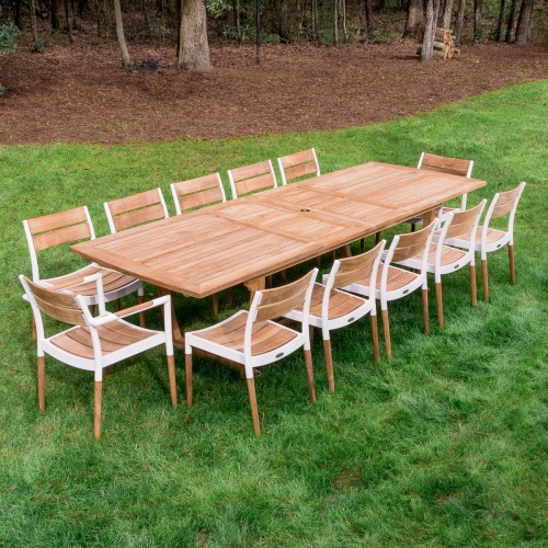 70453 Grand Veranda Bloom 13 piece Dining Set of Grand Veranda teak rectangular dining table and 2 Bloom armchairs and 10 Bloom side chairs on grass lawn with trees in background
