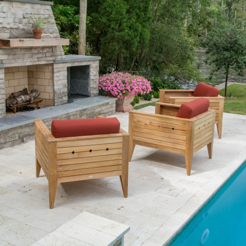 70506 Craftsman three piece teak lounge set on patio facing outdoor fireplace with potted plant on mantle next to pool with potted blooming plant patio edge with trees and grass background