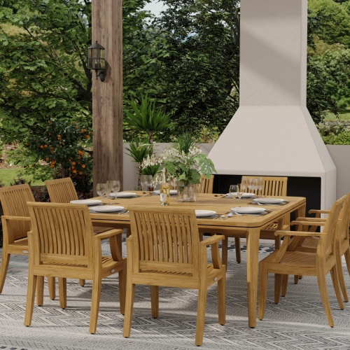 70867 Square Veranda Laguna 9 piece Dining Set of 8 teak dining armchairs and 6 foot square dining table angled view on carpet outdoor patio in front of a fireplace surrounded by plants 