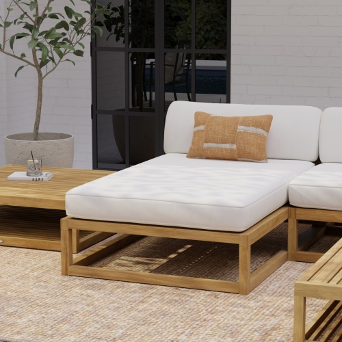 16800DP Maya teak chaise daybed with canvas colored cushion on rug in an outdoor patio against a house with potted plant and window in background