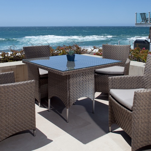 32002SG Valencia Woven 40 inch Square Table with potted plant on glass table top with 4 Valencia Armchairs on outdoor terrace with house in back overlooking ocean and blue sky
