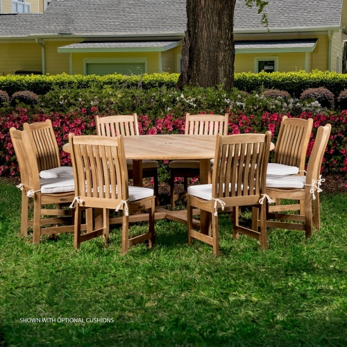 70020 Buckingham Veranda 9 piece teak Dining Set of 8 teak side chairs and  72 inch round table on grass with flowering shrubs and landscaped background