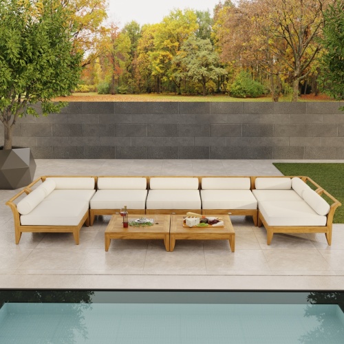 70348 Aman Dais 9 pc Lounge Set with bolsters and cushions angled aerial view on pool deck with privacy wall and trees in background