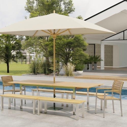 70440 Vogue 7 piece Teak and Stainless Steel Picnic Set with optional umbrella in angled side view in front of a pool with landscape plants and trees and patio of home in the background