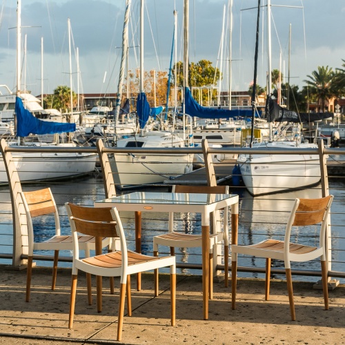 70449 Bloom Glass Top Dining Set of Bloom teak and powder coated aluminum 32 inch square dining table on boat dock and marina with boats and palm trees and blue sky in background