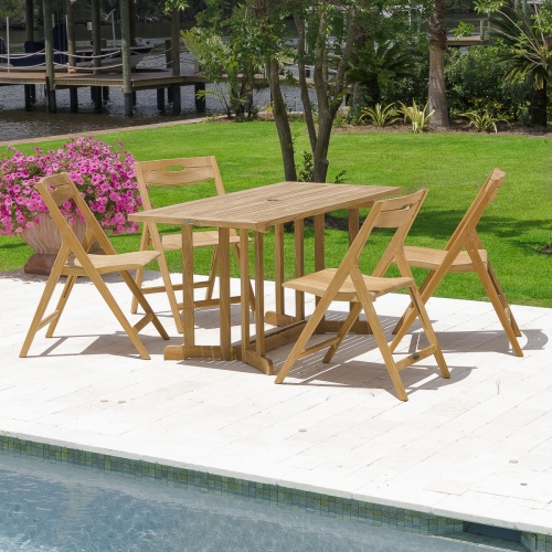 70475 Surf Nevis 5 piece teak rectangular Dining Set on concrete pool patio next to potted flowering plant with grass lawn trees and shrubs a dock and lake in background
