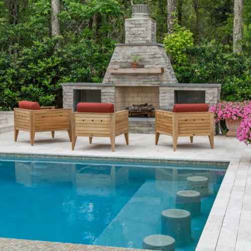 70506 Craftsman three piece teak lounge set on patio facing outdoor fireplace with potted plant on mantle and next to fireplace with pool in front of set and vegetative trees in  background
