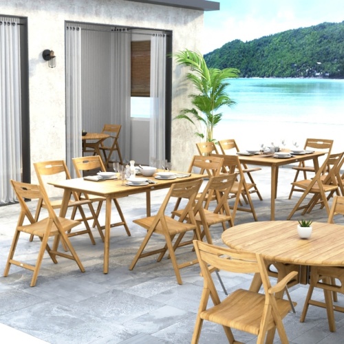 70518 Surf 7 piece teak folding Dining Set showing 2 Dining Sets in hospitality setting on patio with table settings and glasses and potted tree with ocean blue sky and land in background