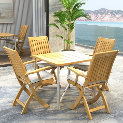 70577 Barbuda Odyssey Folding Dining Set  of Odyssey Table and 4 Barbuda Folding Chairs with optional cushions in corner view on stone patio in front of glass door and potted plant and ocean in background  