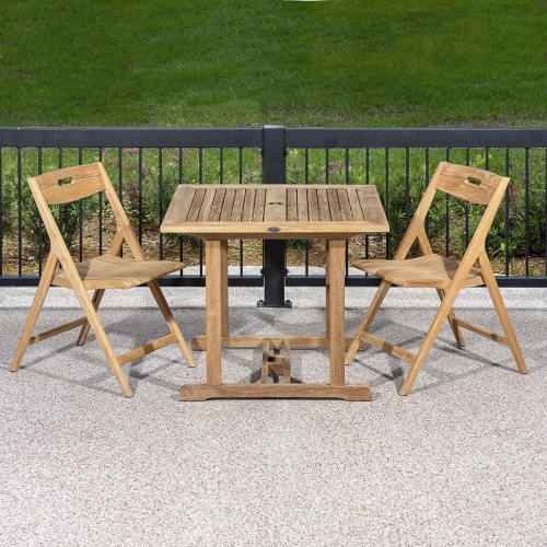70652 Surf Square Teak 3 piece Dinette Set of 2 Surf folding chairs and teak 36 inch square table on patio against a black railing with grass area in background