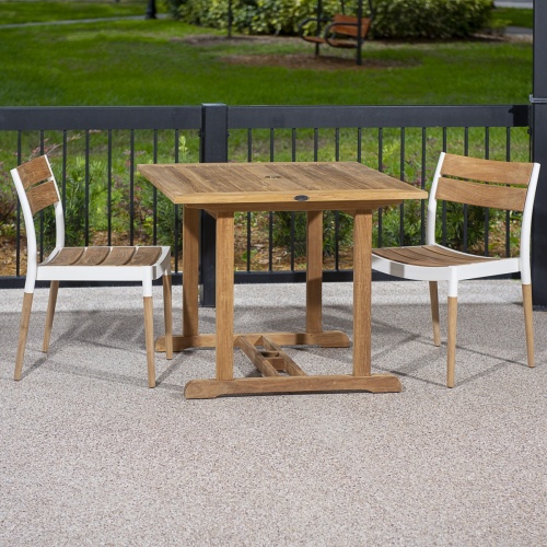 70653 Bloom teak and cast aluminum 3 piece Dinette Set on covered patio against a black railing lined with shrubs with a grass lawn and landscape trees in background 