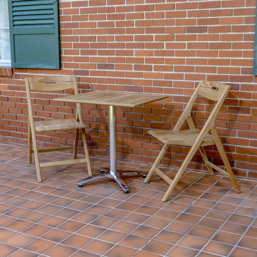 70672 Surf 3 piece teak folding Dining Set of 2 folding teak side chairs and rectangular teak and stainless steel bistro table on patio with brick wall and window shutter in background