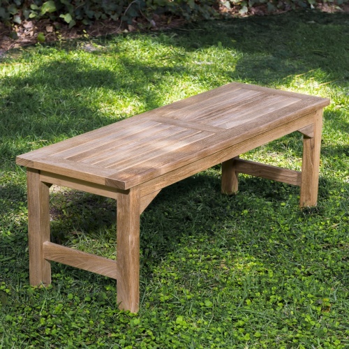13940 Veranda 4 foot Teak Backless Bench angled end view on grass area with trees & shrubs in background