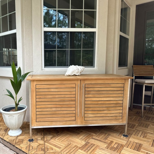 28226 Vogue Teak and Stainless Steel Beverage Console aerial angled view next to a potted plant on tiled outdoor patio with a house and door in the background