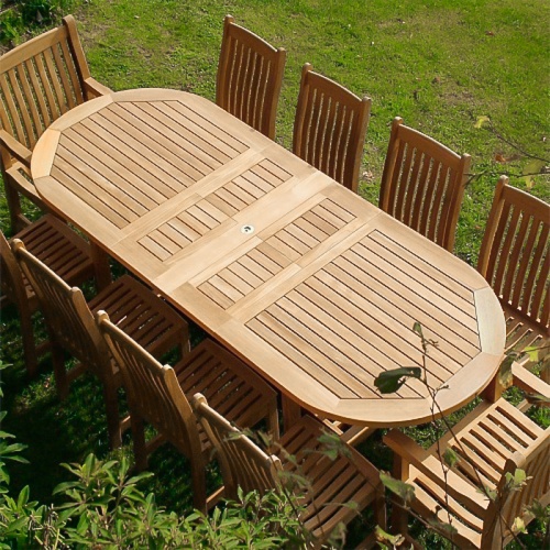 70008 Montserrat Veranda 11 piece oval dining set angled side view on a grass field with palm trees shrubs a boardwalk with 2 lamp posts boat dock and lake in background