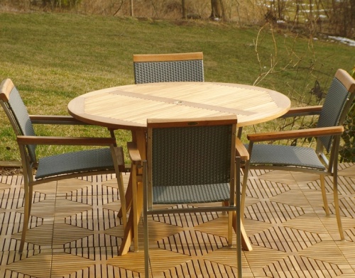 70030 Grand Hyatt SS Kelly Dining Set of a 48 inch round dining table and 4 SS Kelly dining chairs side view on teak tile flooring with grass and trees in background