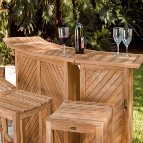 70084 somerset teak five piece bar set fully opened showing two wine glasses and two wine bottles on stone patio facing pool with oak tree and palms in background
