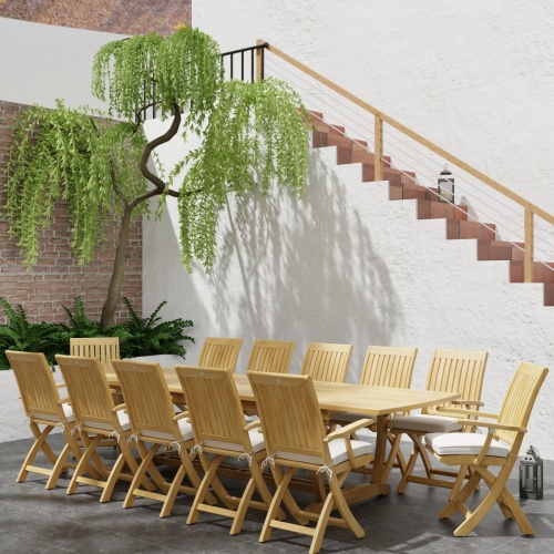 70095 Barbuda Teak 13 pc Patio Set of a Barbuda 10 foot rectangular extension table and 12 folding reclining armchairs in angled with plants next to a staircase in background