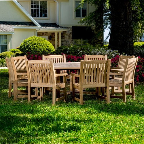 70173 Buckingham 9 pc teak Dining Set with six foot diameter dining table and 8 dining chairs on grass lawn with flowers and tree landscape in background