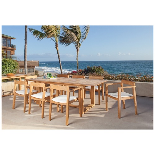 70220 Horizon 9 pc Teak Dining Set of Horizon Rectangular Table and 8 Dining Armchairs in side angled view on patio with 2 columns and house and plant and white fence in background