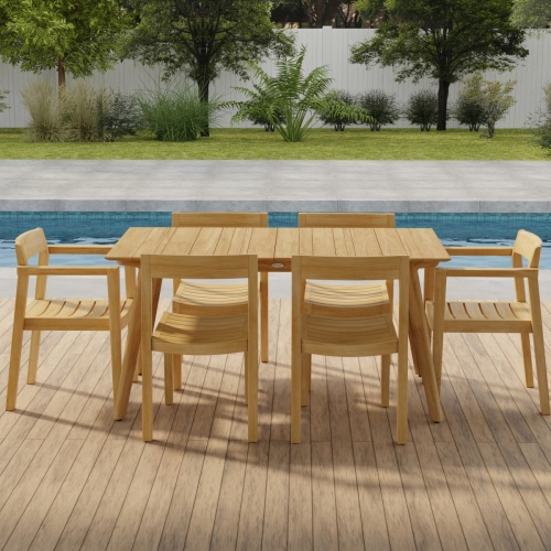 70525 Surf Horizon 7 pc Dining Set of a Surf Teak 60 inch Rectangular Table angled side view on patio in front of a pool with grass and landscaping plants and trees and white fence in the background