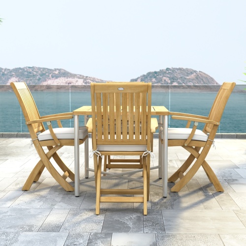 70577 Barbuda Odyssey Folding Dining Set  of Odyssey Table and 4 Barbuda Folding Chairs with optional cushions in side view on stone patio with the ocean and blue sky in background  