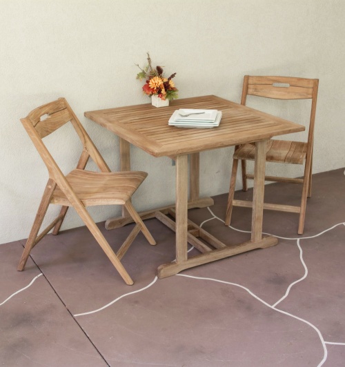 70652 Surf Square Teak 3 piece Dinette Set of 2 Surf folding chairs and teak 36 inch square table with flower arrangement and 4 square white plates on table on patio against a wall