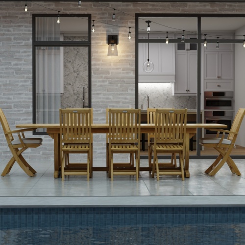 70794 Veranda Barbuda Teak 9 pc Dining Set of Grand Veranda Dining Table and 2 Barbuda Armchairs and 6 Side Chairs side view on a patio with patio lights and glass doors in background