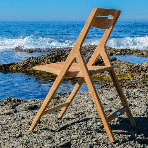 11916 Surf Teak Folding Chair in back angled view on sandy beach facing ocean with blue sky background