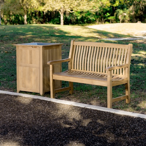 13218 Veranda Teak 4 foot Bench beside teak trash receptacle on grass field with concrete walkway in front and trees in background