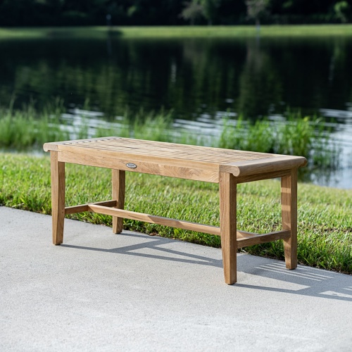 13915 Laguna 4 foot long teak Backless Bench on concrete walkway with grass in background