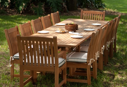 70017 Grand Veranda 13 piece Teak Dining Set with 5 bread plates and 5 salad bowls on table top angled end view on grass field