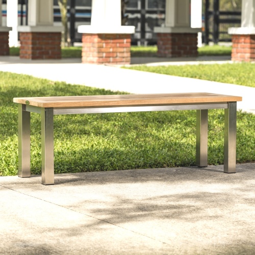  23940 Vogue teak and stainless steel 4 foot backless bench on concrete walkway with grass in background
