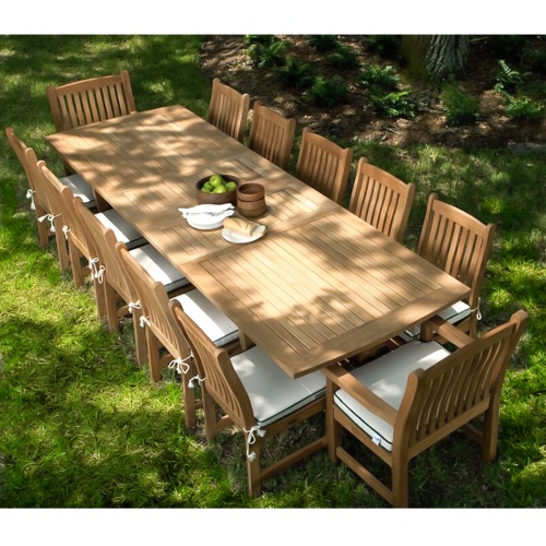 70017 Grand Veranda 13 piece dining set with optional seat cushions a plate of bread serving plates and wooden bowls on a green lawn and lush landscape background