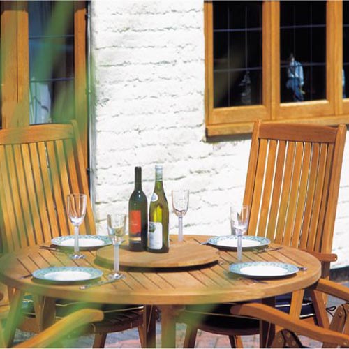 70028 Barbuda Reclining 5 pc Teak Set showing closeup side view with 4 place settings 4 wine glasses and wine bottle on lazy susan with  house windows and glass door in background