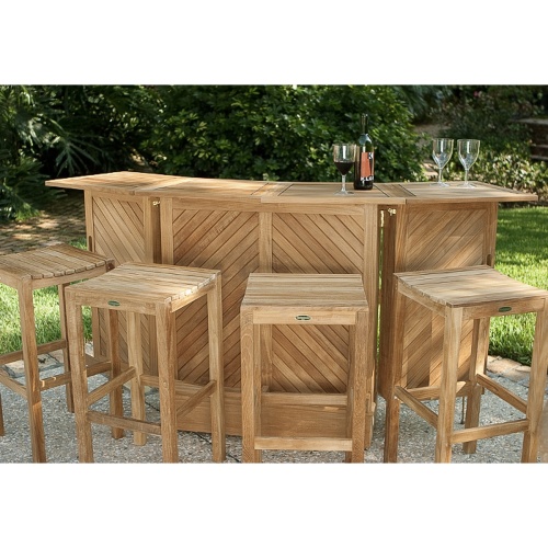 70084 somerset teak five piece bar set showing three wine glasses and wine bottle on top with stone patio a grass area paver walkway and lush tropical plants in background