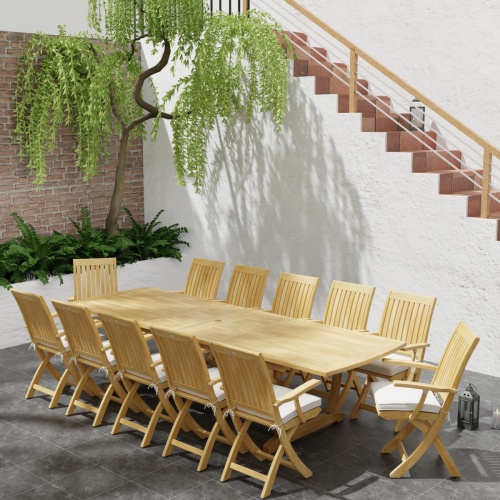 70095 Barbuda Teak 13 pc Patio Set of a 10 foot rectangular extension table and 12 folding reclining armchairs in end angled with plants next to a staircase in background