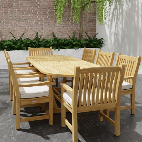 70178 Montserrat Veranda Teak 9 pc Dining Set of Montserrat Dining Table and 8 Veranda Side Chairs in angled side view on outdoor patio with potted plant and staircase of house in the background