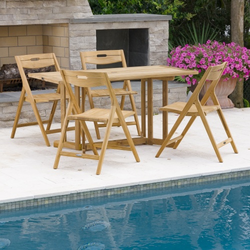70475 Surf Nevis 5 piece teak rectangular Dining Set on concrete patio and pool with flowering plant next to fireplace trees and shrubs in background