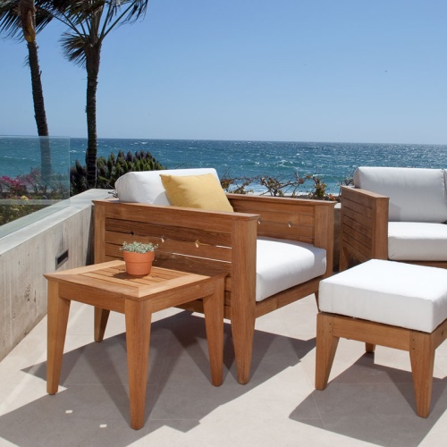 70507 Craftsman 2 lounge chairs with cushions and a teak side table and a teak coffee table ottoman on terrace with palm trees and shrubs and ocean and blue sky background