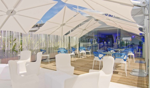 sp2590set spectra solo umbrella and paver base covering tables and chairs on outdoor dining area on wood deck with restaurant in background