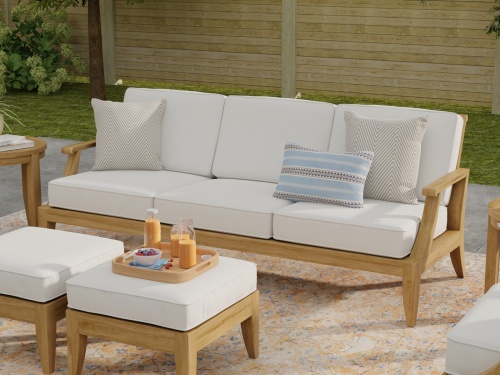13122DP Large Laguna Sofa with 7 pc Conversation Set on patio showing closeup view of Laguna Sofa with throw pillows and 2 ottomans with tray of food with fence in background