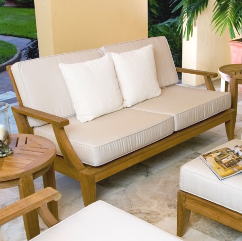 13152dp laguna teak loveseat collection set angled on outdoor patio with candle and holder open magazine potted palm tree with landscaped background