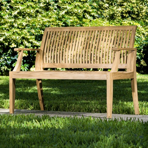 13810 Laguna 4 foot Teak Bench angled on concrete walkway with bushes in background