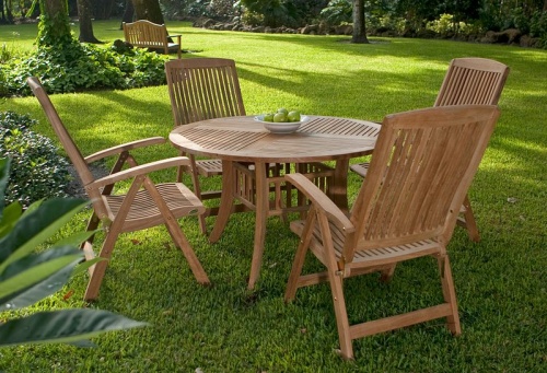 70025 Hyatt Recliner teak 5 piece round Dining Set on grass yard showing a white plate of green apples on table with trees and shrubs in background