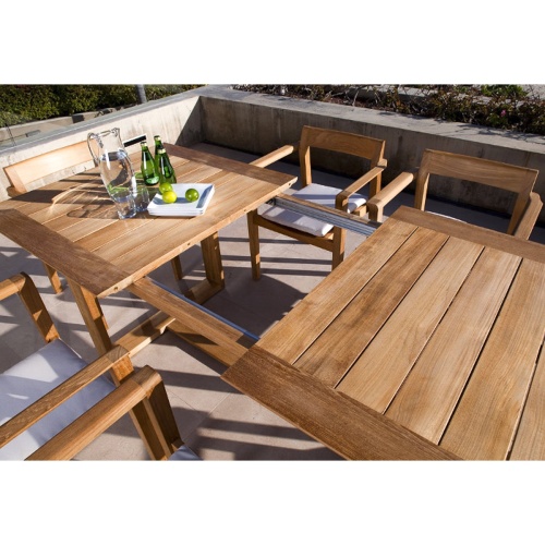 70299 Horizon teak 7 piece Dining Set with 3 sparkling water bottles a water pitcher and plate of oranges on concrete terrace with landscape plants in concrete planter