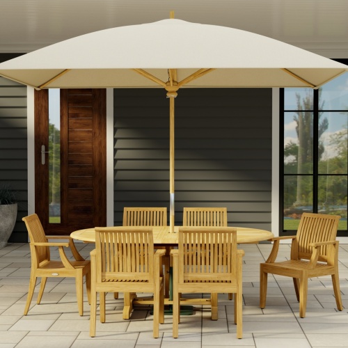 70306 Martinique 7 pc Teak Dining Set of Martinique Teak Oval Extending Dining Table and 6 Laguna DIning Chairs end view on stone patio with 2 pillars of house with a plant and trees and privacy wall in the background  