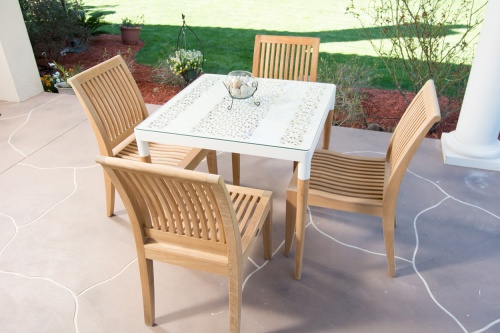 70420 Bloom Laguna teak and powder coated aluminum 5 piece Dining Set on stone patio with round glass vase on table center with landscape plants and grass in background