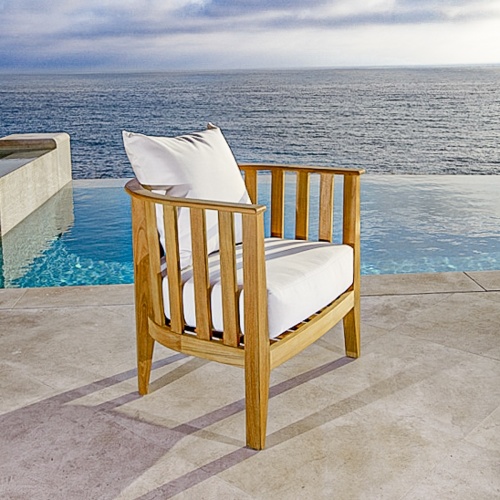 12170 Kafelonia teak Club Chair with cushions side angled on stone patio with pool ocean and blue sky background